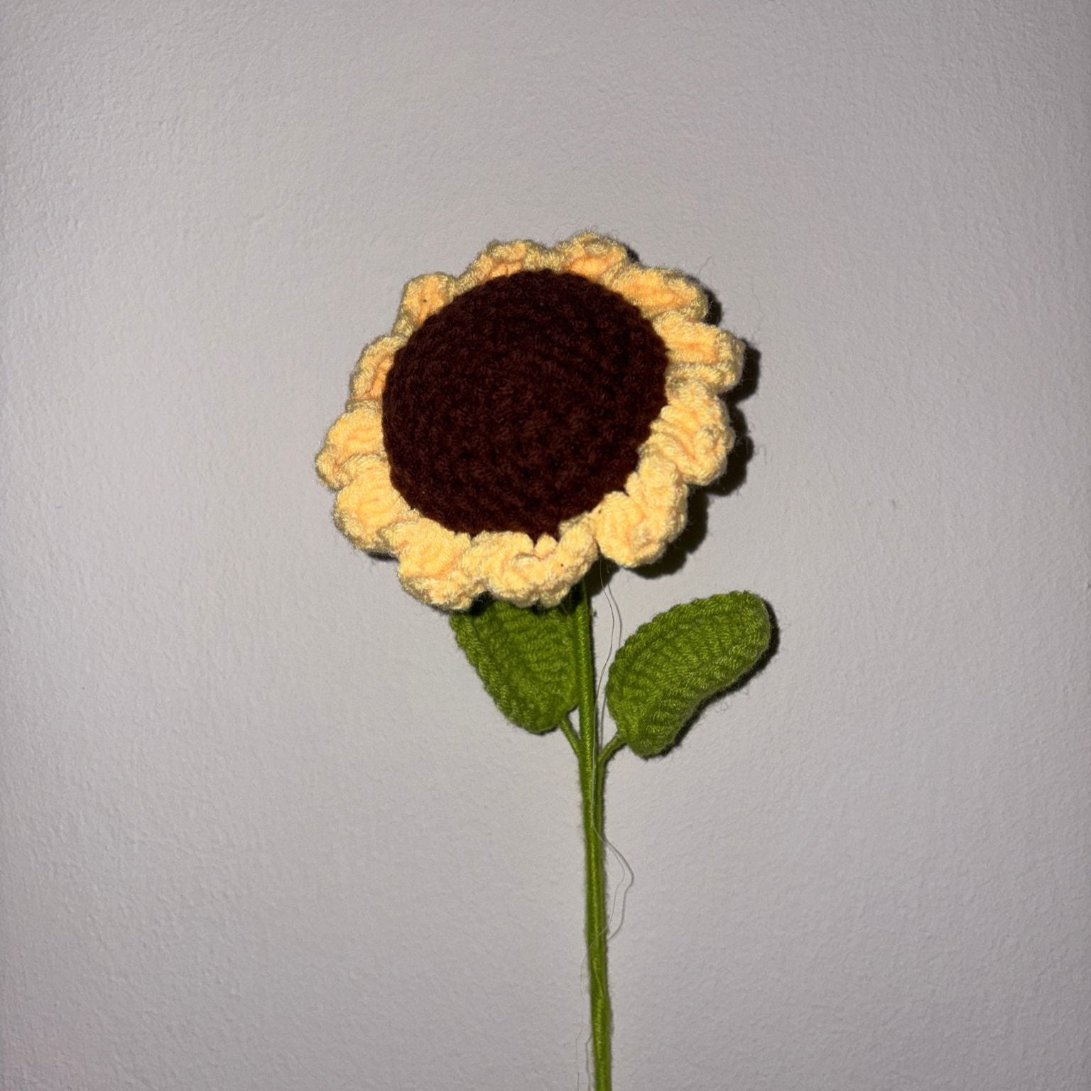Crocheted sunflower with a brown center and yellow petals on a plain background